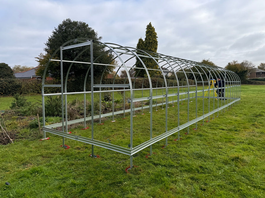 Polyeco Greenhouse frame on a grassy field with ground anchors exposed
