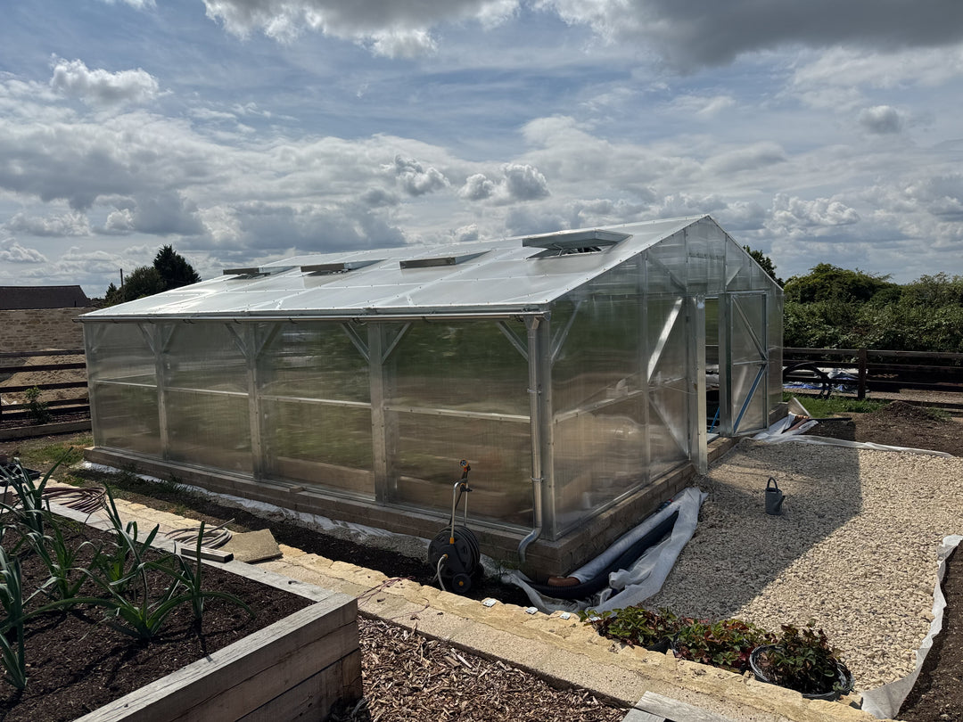 Greenhouse with transparent walls and a metal frame, set against a cloudy sky.
