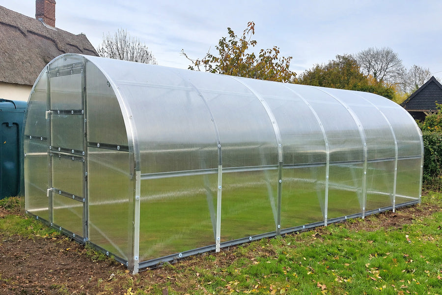 Polycarbonate greenhouse on a grassy area with a house in the background